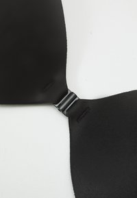 Soutien-gorge noir en tissu lisse et mat. Il présente un fermoir élégant au centre et des bretelles réglables. Design simple, sans motifs visibles.