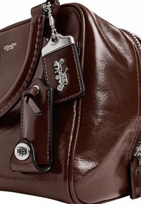 Sac à main Coach en cuir marron foncé brillant avec un charme argenté cheval et carrosse et des détails en métal argenté.