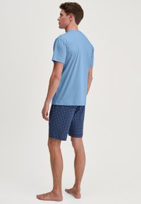 Blauwe katoenen t-shirt gecombineerd met marineblauwe shorts met een wit sterrenpatroon. Het t-shirt heeft een ronde hals; de shorts hebben een elastische tailleband.