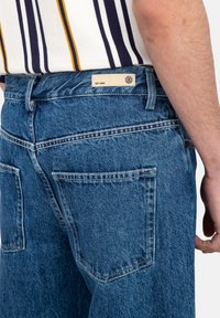 Jeans in denim blu con vita alta e vestibilità rilassata. Presentano dettagli di cucitura, due tasche posteriori e un'etichetta sulla vita.