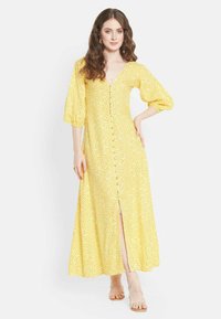Gelbes, gemustertes Maxikleid mit V-Ausschnitt, Puffärmeln, Knopfdetails auf der Vorderseite und einem Schlitz bis zum Oberschenkel. Glatter, leichter Stoff.