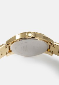 Reloj de acero inoxidable dorado con una caja redonda, corona texturizada y fondo sólido. Presenta un diseño de pulsera de eslabones.