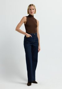 Top sin mangas de color marrón y con canalé, combinado con unos vaqueros de tiro alto de denim azul oscuro. Con características como bolsillos laterales y un ajuste relajado.