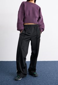 Fialový zkrácený svetr s objemovými rukávy a logem, doplněný o černé široké teplákové kalhoty se bočními kapsami a elastickým pasem.