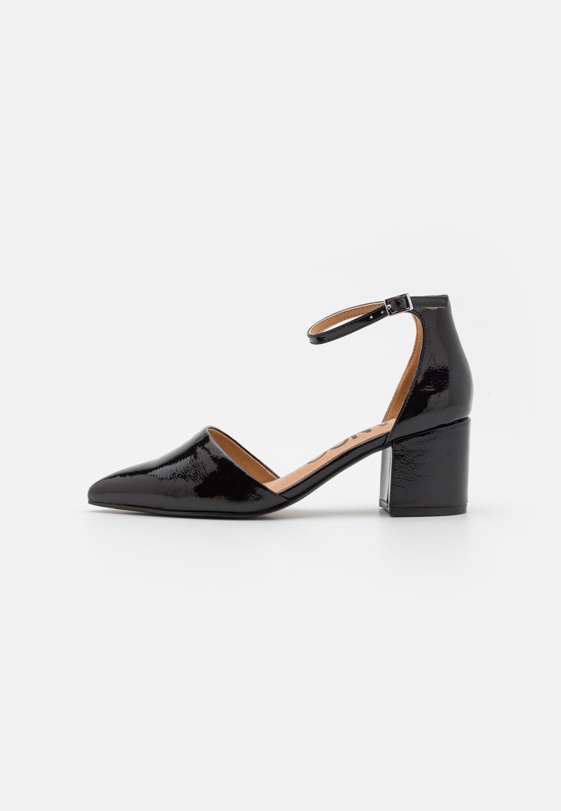 Zapato de charol negro con tacón cuadrado, correa al tobillo, punta afilada y diseño de lado abierto. Textura suave con un acabado brillante.