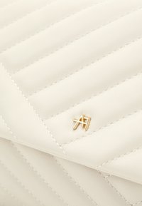 Prošívaná bílá kožená kabelka s diagonálním prošíváním, zdobená zlatým kovovým logem. Hladký povrch a minimalistický design.