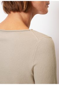 Beiger Strickoberteil mit rundem Ausschnitt und strukturiertem Stoff, mit sichtbaren Nahtdetails an den Schultern und am Rücken.