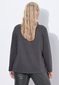 Haut à manches longues gris en tissu doux, avec un col rond et une coupe droite, associé à un pantalon noir élégant.