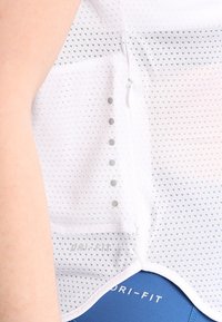 Biała, lekka sportowa koszulka z siateczki z drobnymi perforacjami, zakrzywionym dołem i boczną kieszenią na suwak z odblaskowymi detalami.