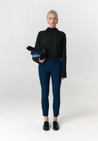 Zwarte top met lange mouwen, nauwsluitende marineblauwe broek, glanzende zwarte schoenen, met een gekreukelde zwarte tas. Gladde stof, op maat gemaakte snit, minimalistische stijl.