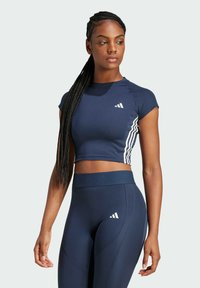 Marine crop top med korte ærmer og hvide sidelommer, parret med højhalsede marine leggings med strukturerede paneler og logo-detaljer.