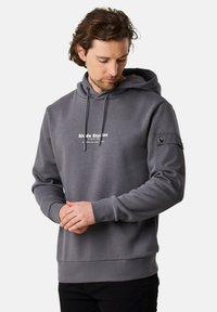 Felpa grigia con cappuccio, logo frontale, polsini a costine e tasca a toppa con dettaglio a bottone sul manica. Tessuto morbido.