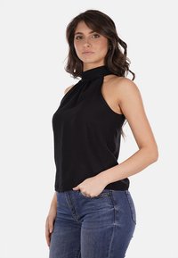 Top nero a halter con collo alto, texture morbida, design aderente e dettagli di drappeggio sottile; abbinato a jeans in denim blu.