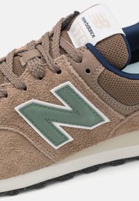 Bruna mockaskons med en grön gummilogga "N", texturerade meshdetaljer, platta snören och en vit mellansula. Har en vadderad krage och tungspets.