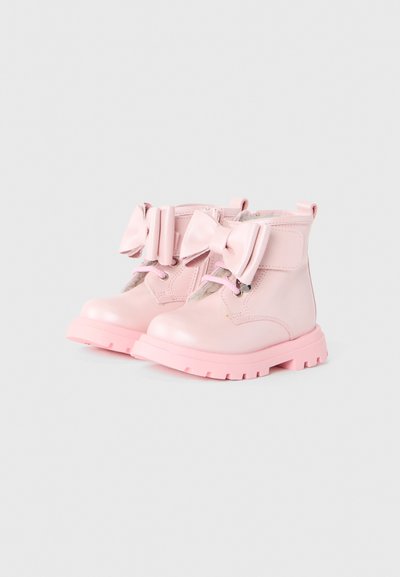 Bottes de cheville en cuir rose avec de grands nœuds et semelles crantées roses. Comprend des œillets pour les lacets et une fermeture éclair sur le côté. Texture lisse.