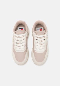 Zapatillas deportivas de color rosa claro con parte superior texturizada, acentos en color crema, cordones blancos y una etiqueta con el logo en la lengüeta. Presenta una puntera redondeada y una suela acolchada.