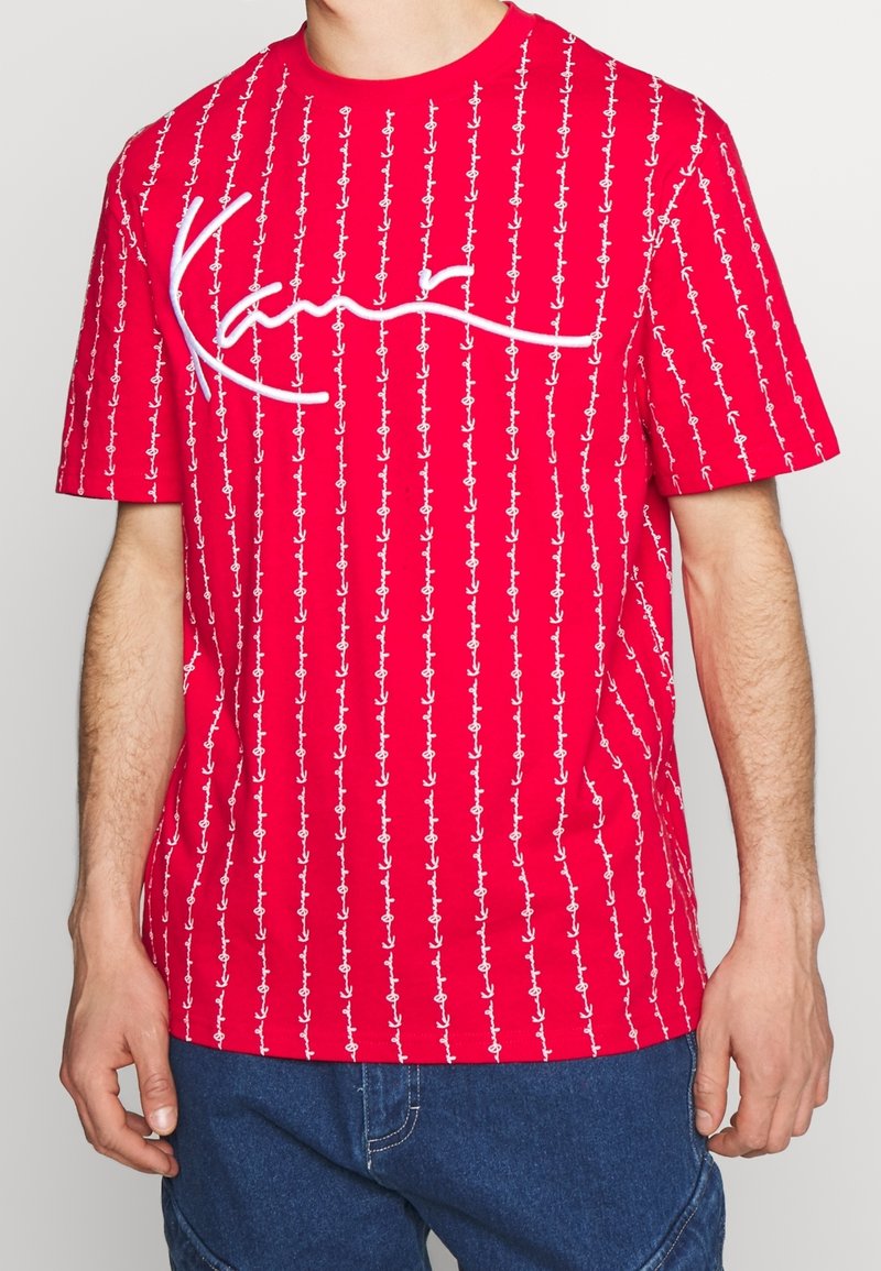 Röd t-shirt med kort ärm, vit ankarmönster och en texturerad, broderad logotyp över bröstet, med en avslappnad passform och rundad halsringning.