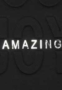 Zwart textuur materiaal met reliëfletters; "AMAZING" in glanzend zilver, contrasterend tegen de matte achtergrond.