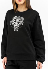 Felpa nera con un grande logo bianco con ali e una corona. Tessuto morbido con polsini e orlo a coste. Design a vestibilità ampia.