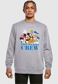 Felpa grigia a girocollo con grafiche colorate di personaggi Disney, tra cui Mickey, Minnie, Donald e Goofy. Il testo recita "Disney CREW."