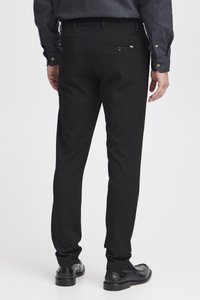 Pantalon noir avec une coupe élégante et slim. Fabriqué à partir d'un tissu lisse, il présente des poches arrière et un motif subtil le long des bords des poches.
