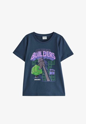Vaalea lapsi, jolla on yllä Minecraft Buildersin tummansininen T-paita, ruskeat shortsit valkoisilla raidoilla, valkoiset lenkkarit ja pidellen Minecraft-lippistä.