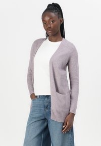 Helllila Strickjacke aus weichem Material, mit offener Vorderseite, gerippten Bündchen und einer Vordertasche, getragen über einem weißen Oberteil und Jeans.