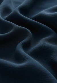 Marinblått tyg med en slät, flödande textur, med mjuka vågor och subtil lyster, vilket indikerar ett lätt material.