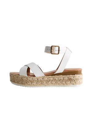 Sandalia blanca de cuña con correa al tobillo, suela de plataforma de yute trenzado y hebilla dorada sobre fondo blanco.