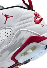 Sneaker in pelle bianca con dettagli rossi, superficie texturizzata, cuciture visibili, lato perforato e una funzione di ammortizzazione trasparente.