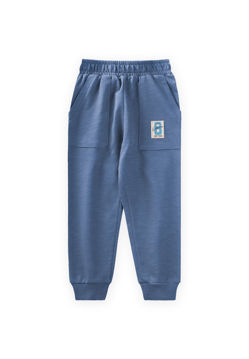 Blaue Jogginghose aus weichem Stoff, mit seitlichen Taschen, elastischem Bund und gerippten Bündchen. Ein Etikett mit der Nummer 8 ist angebracht.