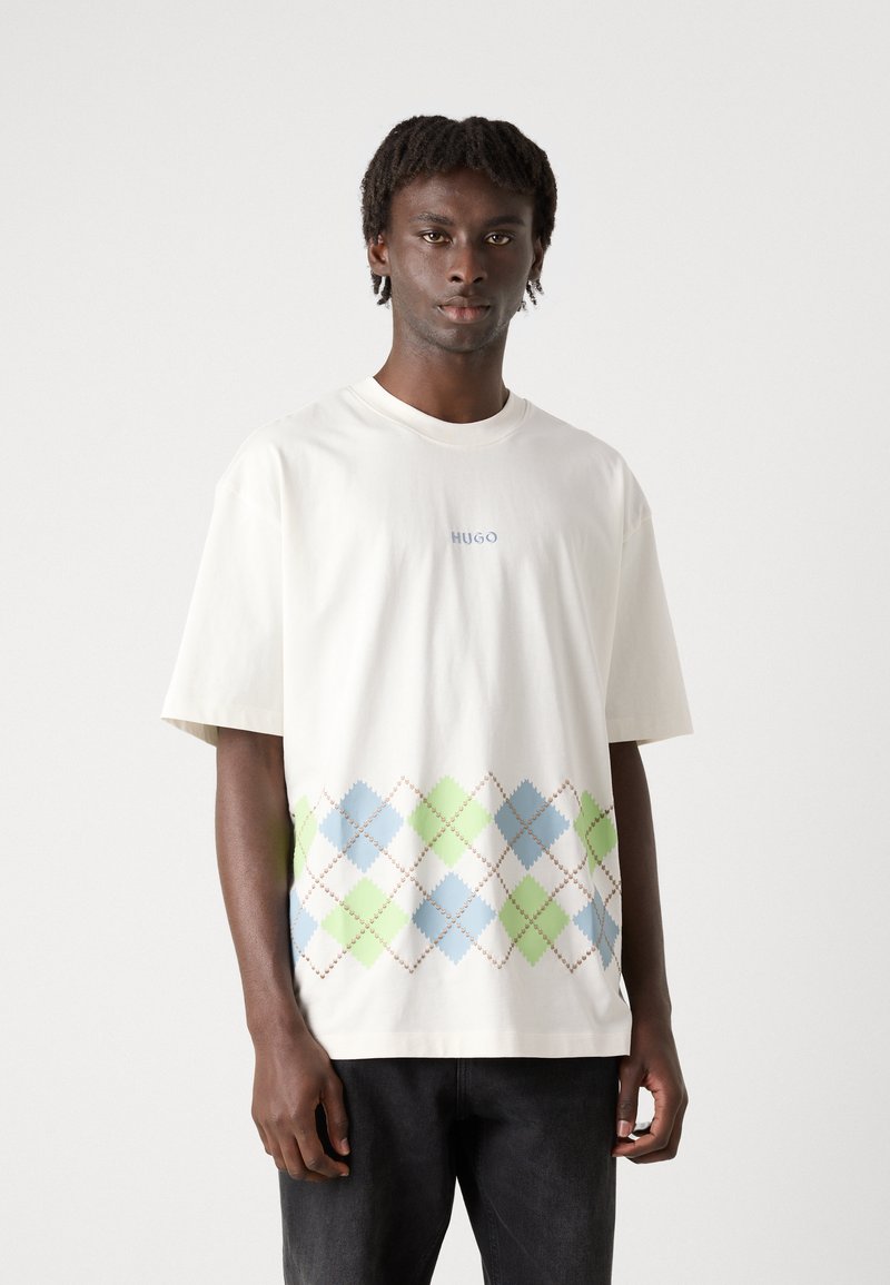 Biały bawełniany T-shirt z kolorowym wzorem w argyle w odcieniach niebieskiego, zielonego i brązowego na dolnej części, z napisem "HUGO" powyżej wzoru.