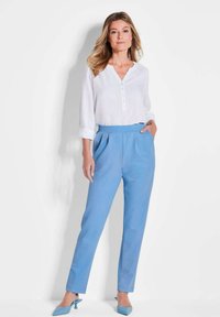 Weiße Langarmhemd mit Knöpfen, kombiniert mit hellblauen maßgeschneiderten Hosen und passenden blauen High Heels; glattes Material mit dezentem Glanz.