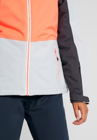 Windbreaker-Jacke in Grau, Orange und Schwarz. Mit einem Front-Reißverschluss, Seitentaschen und kontrastierenden Farbkombinationen. Glatte Textur.