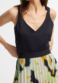 Top negro sin mangas con escote en V y dos tirantes, combinado con una falda plisada que presenta un patrón abstracto colorido en tonos pastel.