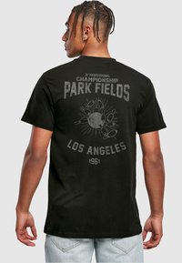 Must have mustris t-särk mustas värvitoonis, millel on suur hall vintage trükk seljal. Kujundus sisaldab "PARK FIELDS", keegli pinde ja "LOS ANGELES 1961".