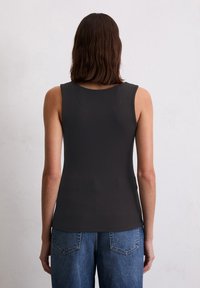 Débardeur noir à côtes avec un col rond et une conception sans manches, associé à un jean bleu taille haute avec des poches arrière.