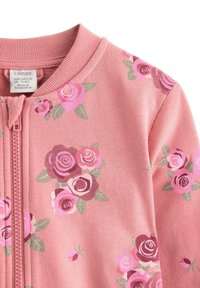 Różowa dziecięca kurtka zapinana na zamek z kwiatowymi wzorami w odcieniach fioletu i zielonych liści, metka z rozmiarem widoczna w pobliżu kołnierza.