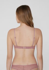 Roze kant bralette met verstelbare bandjes, een haak-en-oogsluiting, met bloempatronen langs de band en een zachte stoftextuur.