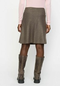 Jupe évasée marron en tissu texturé, tombant juste au-dessus du genou, assortie à de hautes bottes en cuir marron.