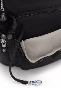 Black fabric backpack with a grey lined pocket. Features a keychain of a black monkey figure and silver hardware accents.