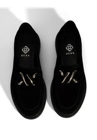 Black suede loafers with a smooth texture, featuring a metal accent strap, rounded toe, and embossed logo on the insole.