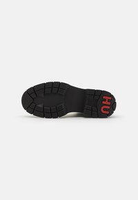 Talpa de pantofi din cauciuc negru cu tălpi profunde pentru tracțiune, brand embosat și o bază netedă și rezistentă. Accente roșii pe călcâi.