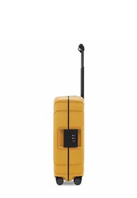 Maleta amarilla de carcasa rígida con cremallera negra, candado de combinación negro empotrado, mango telescópico negro extensible y cuatro ruedas negras, en posición vertical.
