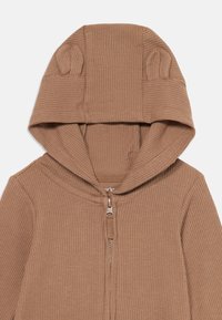 Children’s brown waffle-knit zip-up hoodie with small fabric bear ears on the hood.