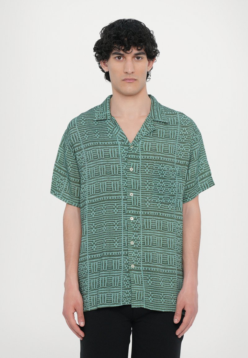 Camisa de mangas curtas, com colarinho, na cor verde com padrões geométricos, apresentando botões na frente e uma textura de tecido leve.