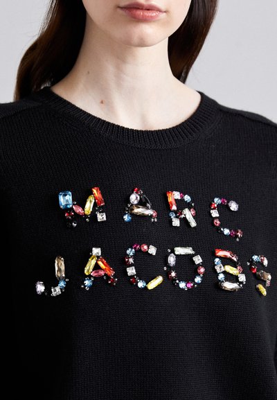 Pulover negru tricotat, decorat cu bijuterii colorate care formează cuvântul "MARC JACOBS". Bijuteriile variază în formă și dimensiune, adăugând textură și detaliu.