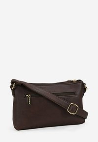 Bolso cruzado de cuero marrón con una textura suave, que cuenta con dos bolsillos con cremallera y una hebilla de correa dorada. Diseño compacto y práctico.