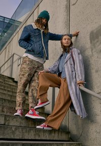 Due persone su una scala vestite in modo casual. L'uomo indossa una giacca di jeans, pantaloni mimetici e sneaker rosse; la donna indossa un cappotto a righe e pantaloni marroni.