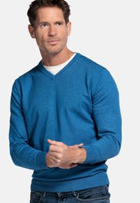 Blauwe v-hals trui van zachte breiweefsel. Gemaakt met lange mouwen met geribbelde manchetten en een aansluitende tailleband. Eenvoudig ontwerp zonder patronen.